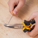 A hand holding a pair of Tolsen 1600mm bent nose pliers, gripping a coiled metal wire on a wooden surface