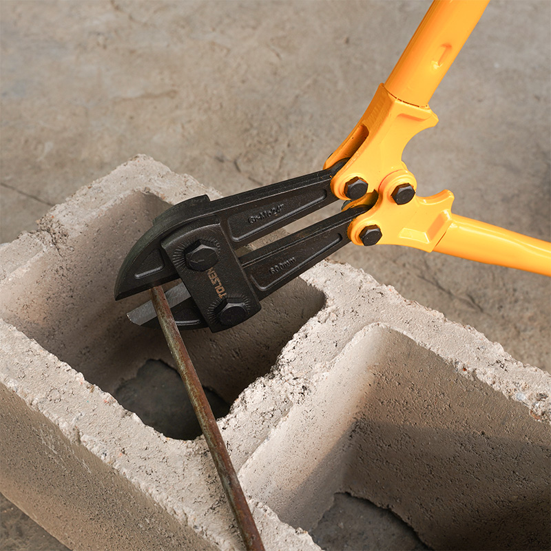 Close-up of Tolsen 24 inch bolt cutter cutting metal rod on concrete block