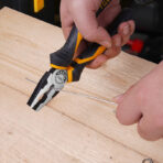 Close-up of hand using Tolsen 6-inch combination pliers to cut wire on a wooden surface