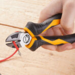 Close-up of hand using Tolsen 6-inch diagonal cutting pliers to cut red electrical wire on a wooden surface