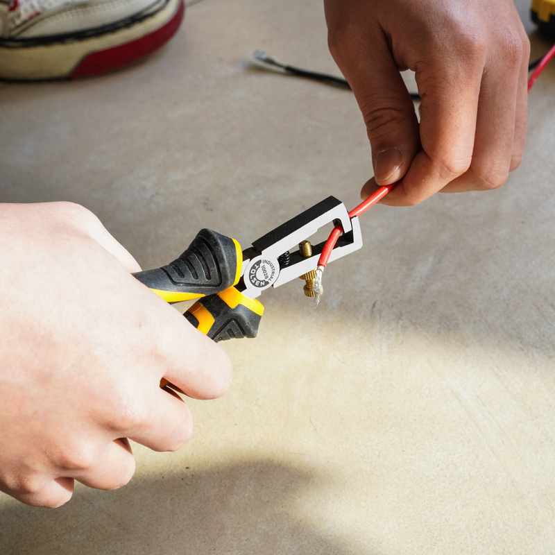 Close-up of hand using Tolsen 6-inch industrial wire stripping pliers to strip insulation from electrical wire