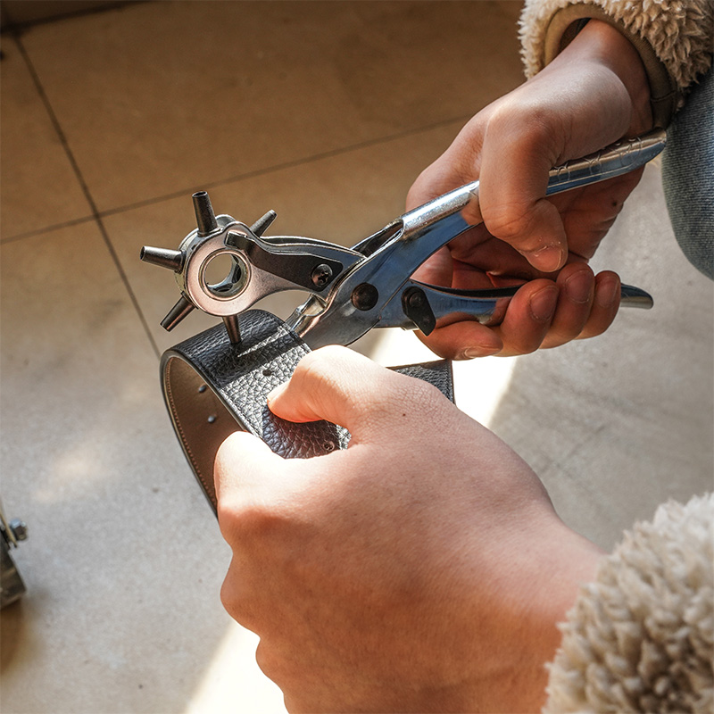 Close-up of hand using Tolsen 9 inch revolving punch pliers to punch a hole in a leather belt