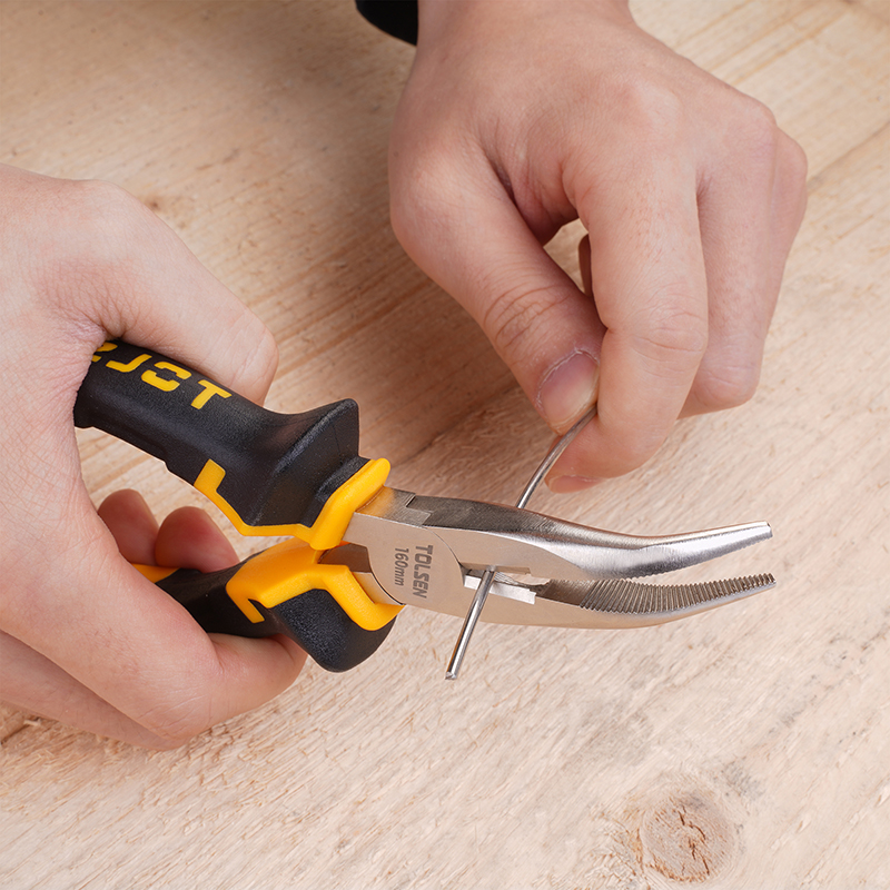 Close-up of hands using Tolsen 160mm bent nose pliers to cut a piece of metal wire on a wooden surface