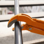 Close-up of Tolsen 45 degree bent nose pipe wrench gripping metal pipe