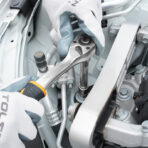 Close-up of hand wearing grey gloves using Tolsen ratchet and socket to tighten a bolt on a car engine component