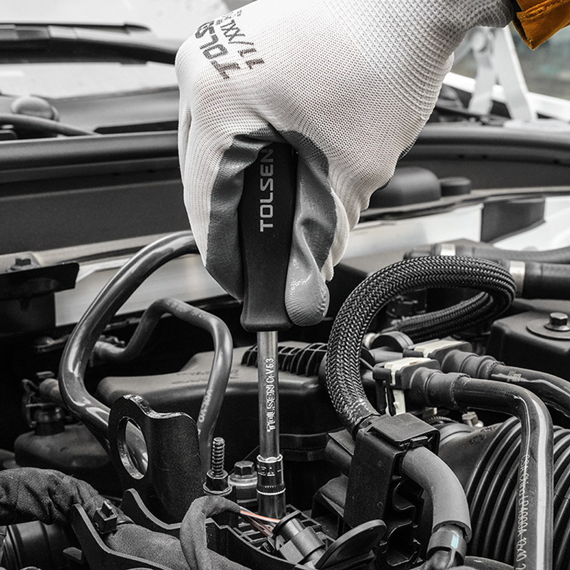 Hand wearing glove using Tolsen screwdriver and socket to work on car engine, close-up