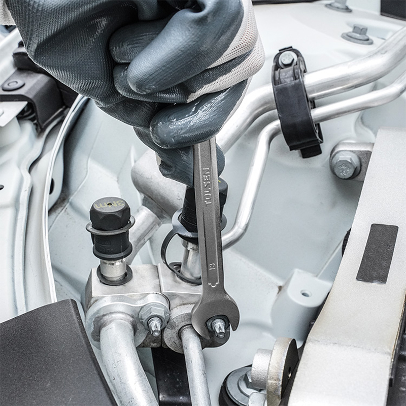 Hand wearing glove using Tolsen wrench to tighten bolt in car engine compartment, close-up