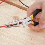 Close-up of Tolsen 6 inch long nose pliers cutting red wire on wooden surface